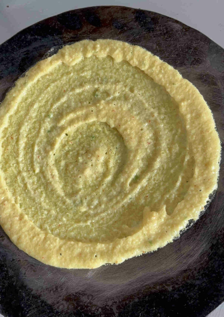 spread moong dal batter on iron tawa for making chilla